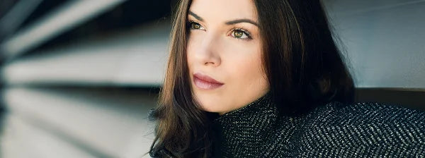 Woman with long brown hair looking thoughtfully to the side, wearing a dark textured sweater